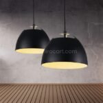 Two black Fjord Halo pendant lights with gold interiors glow warmly against a concrete wall in an industrial-style space.
