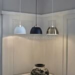 Three Fjord Halo pendant lights—blue, black, and silver—hang in unison, adding a playful contrast to a soft neutral interior.