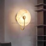 Gold-framed Moonlit Alabaster Wall Light mounted near modern shelving, exuding warm elegance.