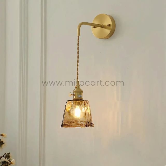 Golden vintage wall light with a glass shade on a crisp white wall, glowing softly.
