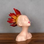 Feminine resin sculpture with fiery red and yellow crown, seated gently on a warm wooden surface.