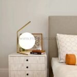 Minimalist gold sphere table lamp on a nightstand, softly lighting a tranquil bedroom.
