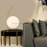 Minimalist gold sphere table lamp on a side table next to a sleek sofa.