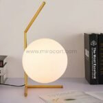 Minimalist gold sphere table lamp on a study desk beside books and notes.