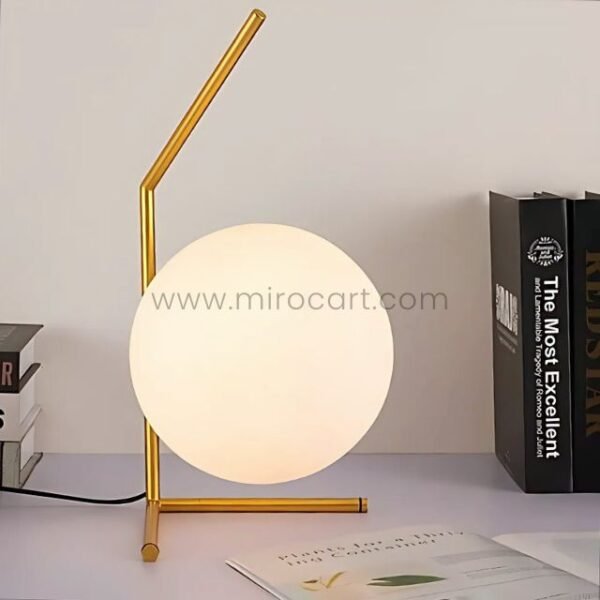 Minimalist gold sphere table lamp on a study desk beside books and notes.