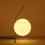 Minimalist gold sphere table lamp glowing against a warm orange background.