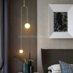 Gold modern arc pendant light with dual globes in a minimalist bedroom.