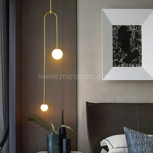Gold modern arc pendant light with dual globes in a minimalist bedroom.