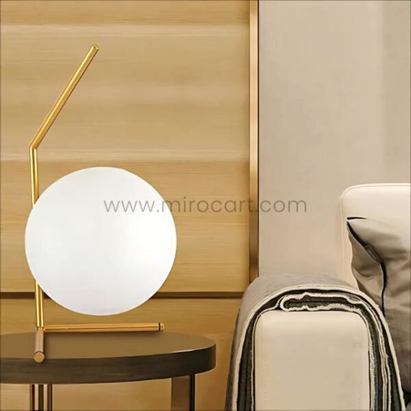 Minimalist gold sphere table lamp on a side table beside a modern bed.