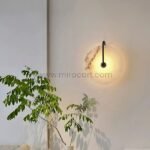 Black-framed alabaster wall light near leafy greenery, casting a soft, natural glow.