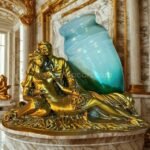 Gold-toned sculpted lovers figurine with opaline glass vase displayed in a richly decorated living room with velvet drapes and ornate details.