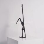 Black metal sculpture of a human figure in a handstand pose, viewed from the side, showcasing its elegant lines and balanced form.