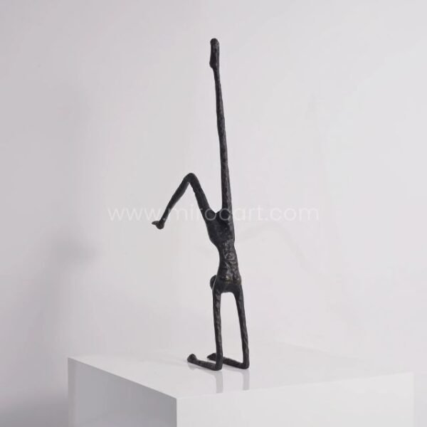 Black metal sculpture of a human figure in a handstand pose, viewed from the side, showcasing its elegant lines and balanced form.