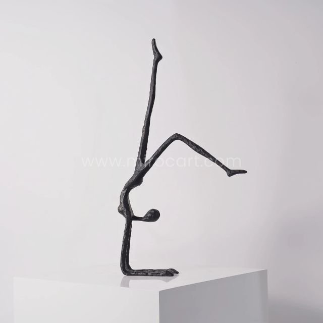 Sleek black metal sculpture of a human figure performing a handstand, displayed on a white pedestal against a clean, neutral background.