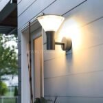 Modern outdoor wall light with black housing mounted on residential siding.