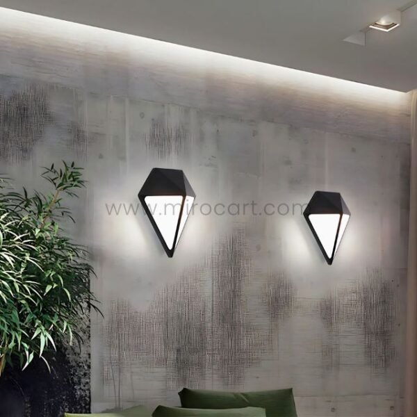 Two diamond wall lights glowing warmly on a textured rustic wall, lighting a leafy outdoor seating area.