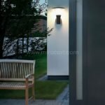 Modern outdoor wall light installed near a wooden bench, casting light across a quiet seating area.