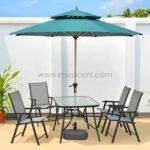 Modern outdoor table set with teal umbrella, glass-top table, and foldable chairs on a sunlit patio