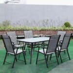 Modern outdoor table set with glass top and foldable chairs on green surface.