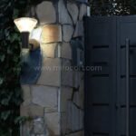 Modern outdoor wall light with black finish mounted beside a stone gate wall.