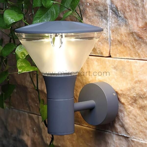 Modern outdoor wall light with sleek gray design mounted on a stone wall, surrounded by greenery.