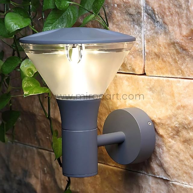Modern outdoor wall light with sleek gray design mounted on a stone wall, surrounded by greenery.