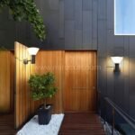 Two modern outdoor wall lights on either side of a wooden entry door, casting warm light.