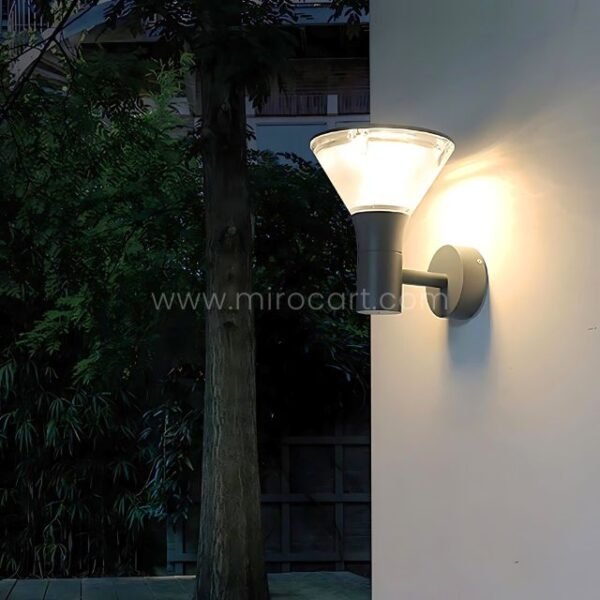 Gray modern outdoor wall light mounted on a white garden wall surrounded by plants.