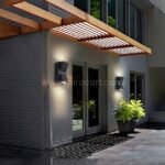 Modern up and down wall lights installed on both sides of an outdoor entry framed with wood and plants.