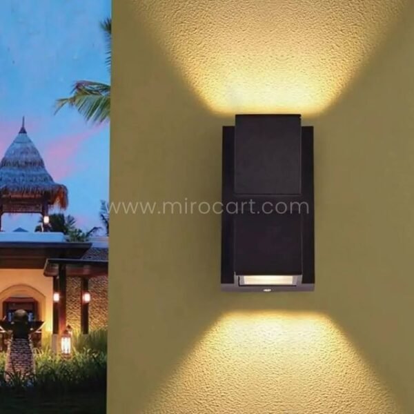 Modern up and down wall light glowing against a textured outdoor wall in a tropical garden.