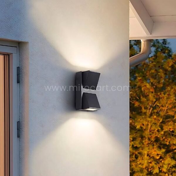 Modern up and down wall light on an exterior wall with trees and greenery nearby.