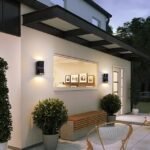 Modern up and down wall lights illuminating a cozy outdoor patio with plants and seating.