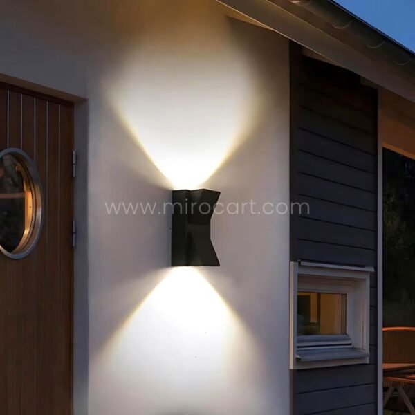 Modern up and down wall light mounted on a textured facade beside a circular front door.