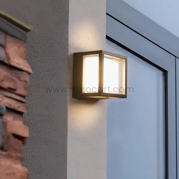 Sleek cube wall light on rustic brick facade near entryway door.