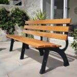 A classic wooden park bench sits on a clean, modern concrete backyard patio near large house windows and minimalist potted plants.
