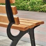 Detailed close-up of a classic wooden park bench highlighting the texture of the light brown wood slats and the smooth, black powder-coated metal frame.
