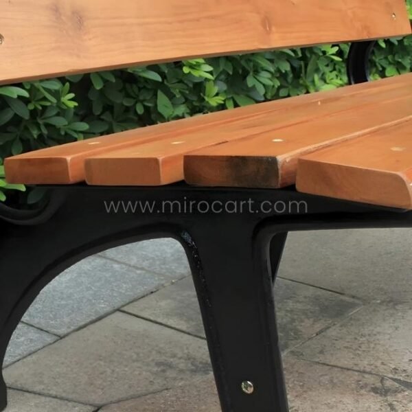 Top-down close-up of the light brown solid wood seat slats of a classic park bench, revealing the black metal support beam for extra stability.