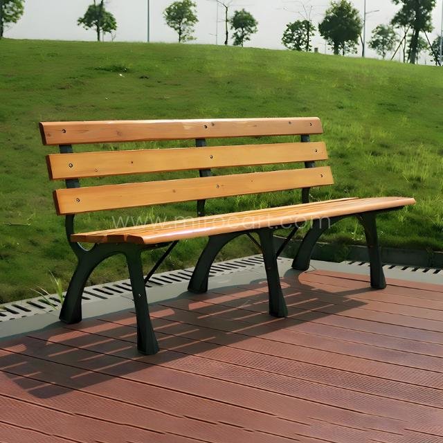 Classic wooden park bench with a light brown solid wood seat and black metal frame, situated on a red composite deck overlooking a green lawn.