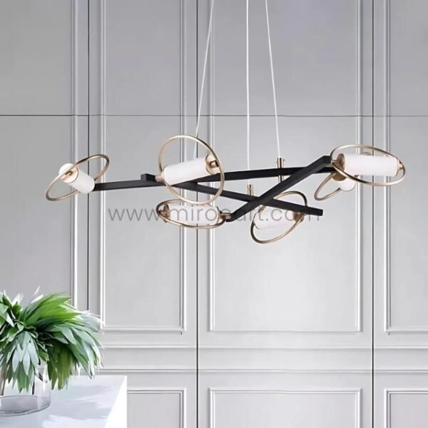 Modern Cross Pendant Chandelier with black frame and gold rings against a white paneled wall with green plant.