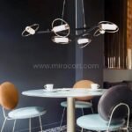 Modern Cross Pendant Chandelier above a round dining table with mid-century chairs in a dark-toned room.