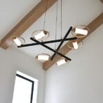 Modern Cross Pendant Chandelier with black metal frame and gold rings in a vaulted ceiling with wooden beams.